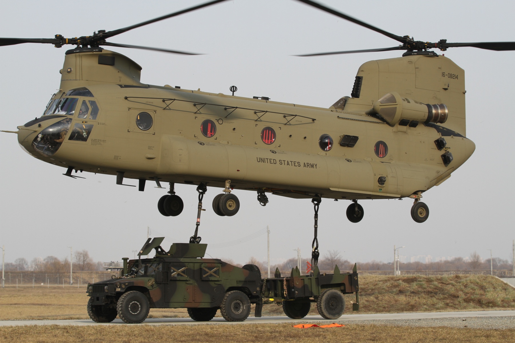 Взлет тяжелого вертолета  CH-47 Chinook 123-го батальона обеспечения Армии США с многоцелевым колесным тягачом с прицепом на внешней подвеске, фото сделано 7 января 2019 года на базе Camp Humphreys, Республика Корея